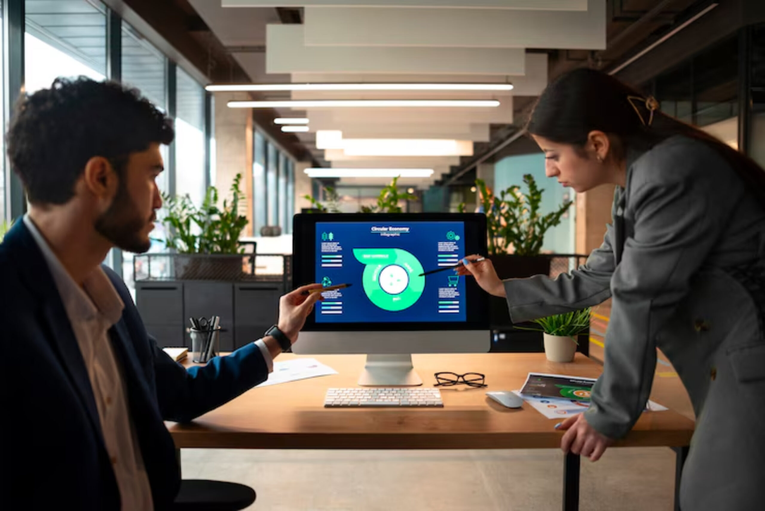 A professional discussion at a modern office, featuring a monitor displaying a circular infographic on the circular economy.