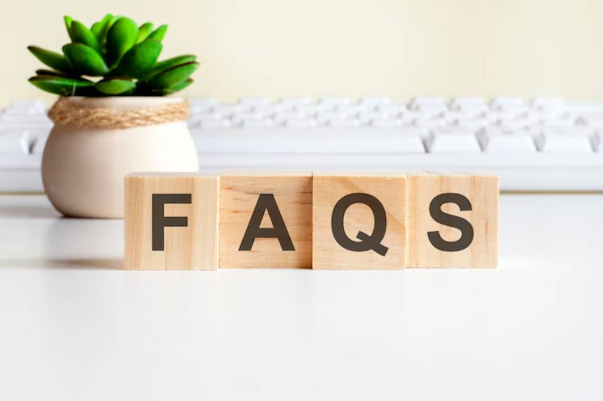 Wooden blocks spelling FAQs on a white desk, with a potted plant and keyboard in the background.