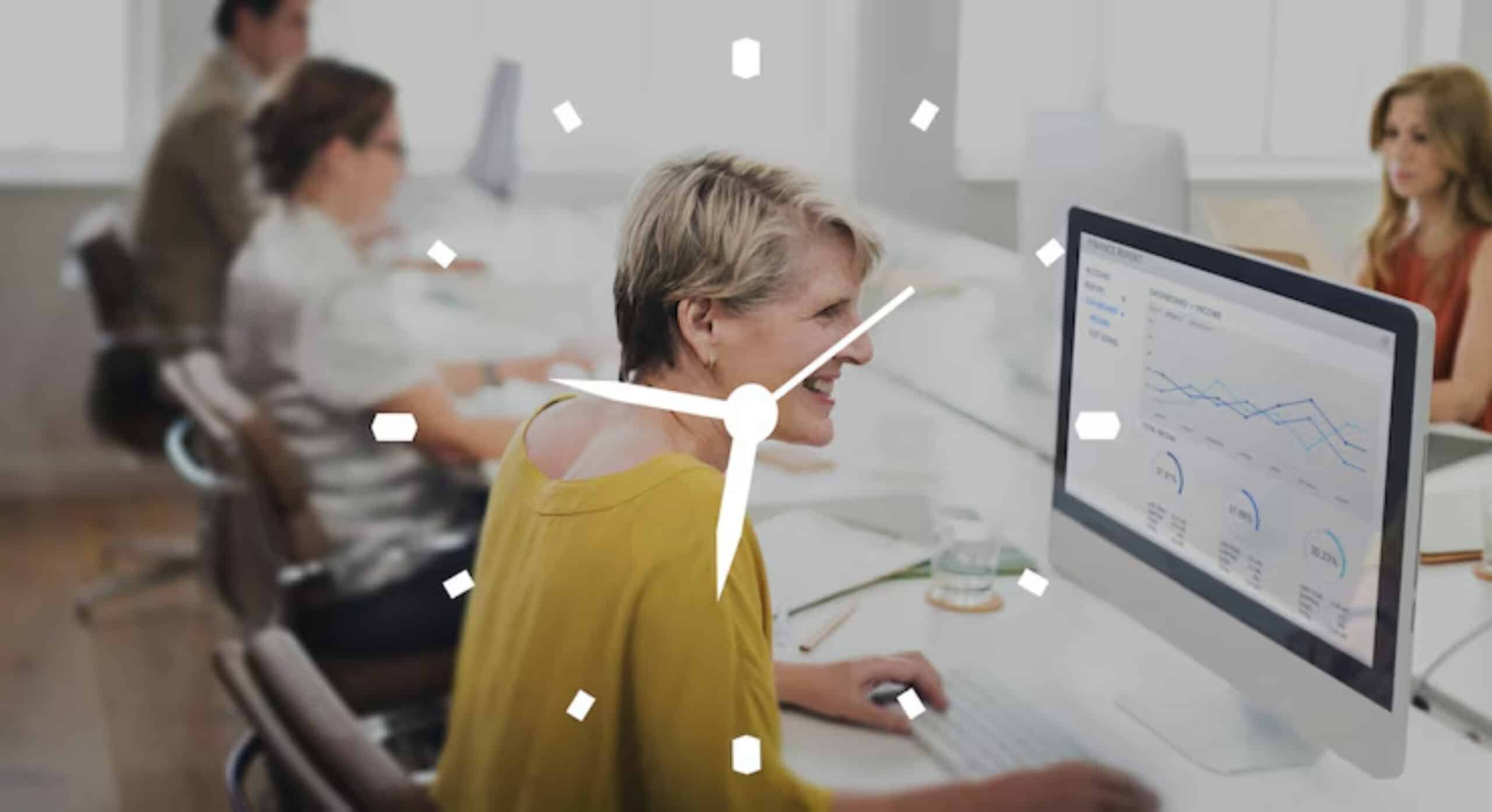 A woman in a yellow shirt works on a computer displaying financial data, surrounded by colleagues in a bright office setting.