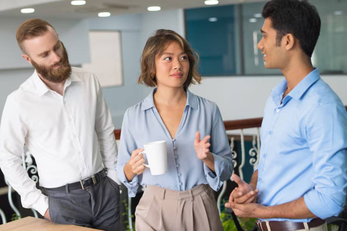 Three professionals engaged in discussion in a modern office setting, one holding a coffee mug while gesturing expressively.