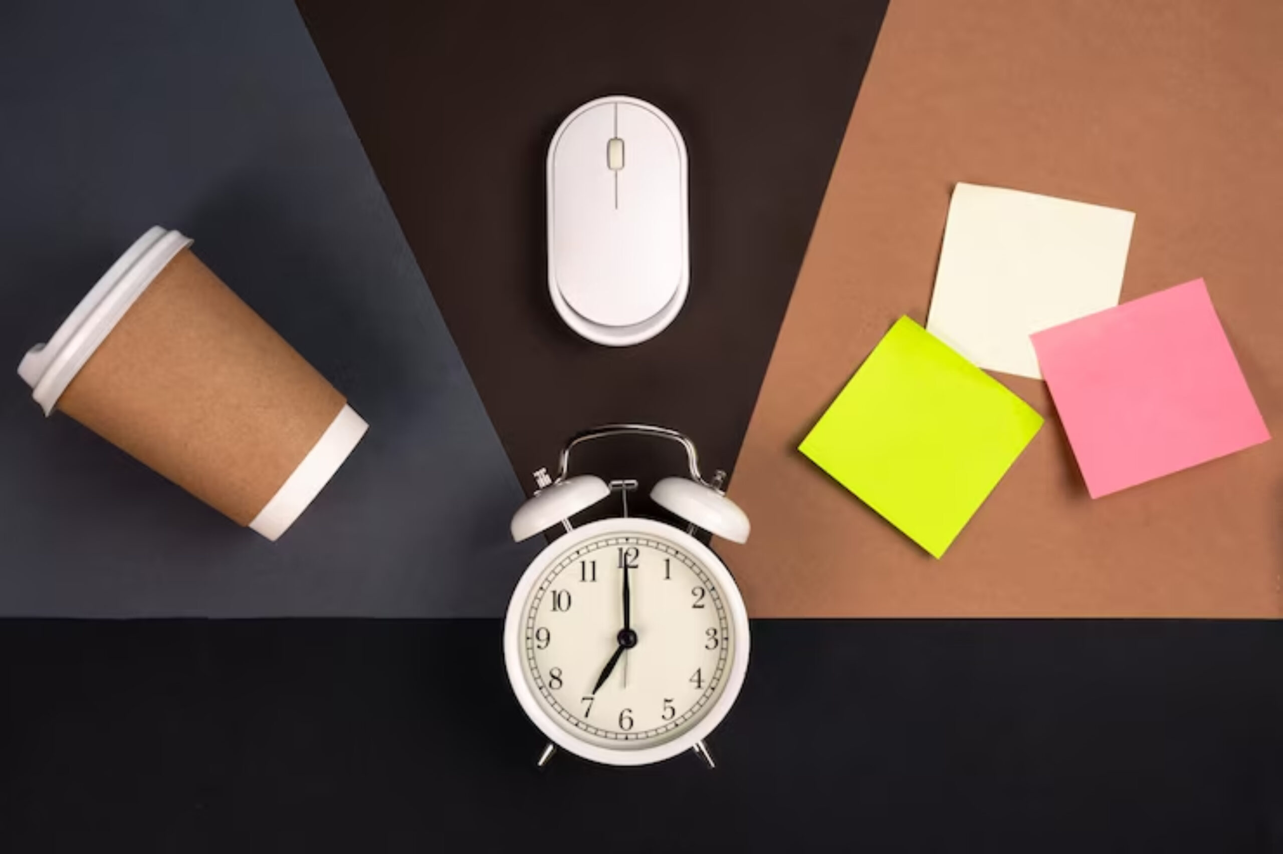 A flat lay of a coffee cup, computer mouse, alarm clock, and colorful sticky notes on a dark and light-colored background.