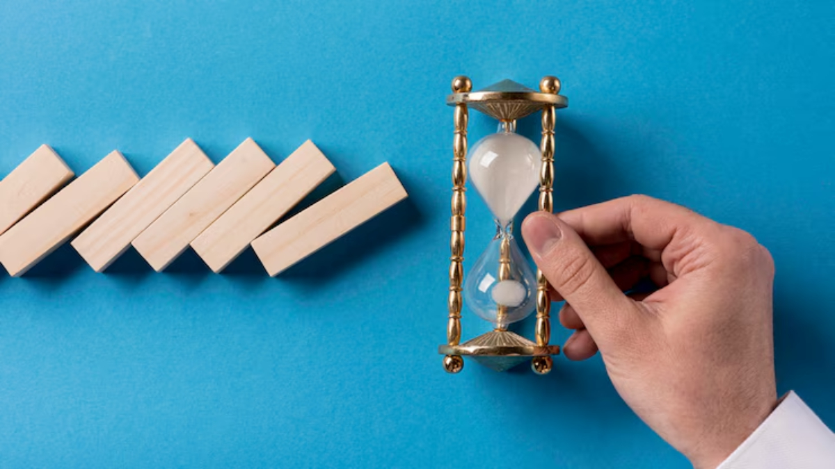 A hand adjusts a golden hourglass next to a row of wooden blocks on a vibrant blue background, symbolizing time management.