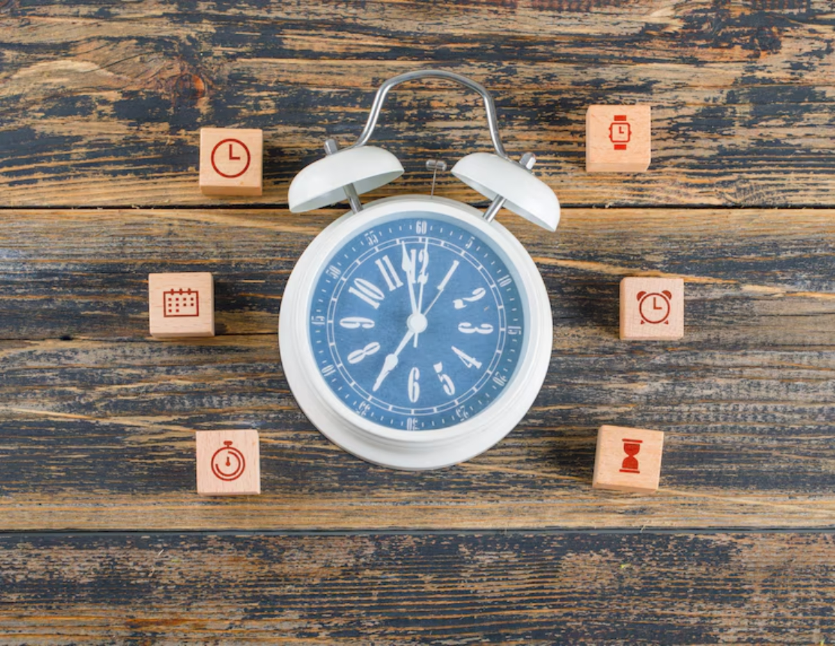 A white alarm clock surrounded by wooden blocks, each featuring clock-related symbols on a rustic wooden surface.